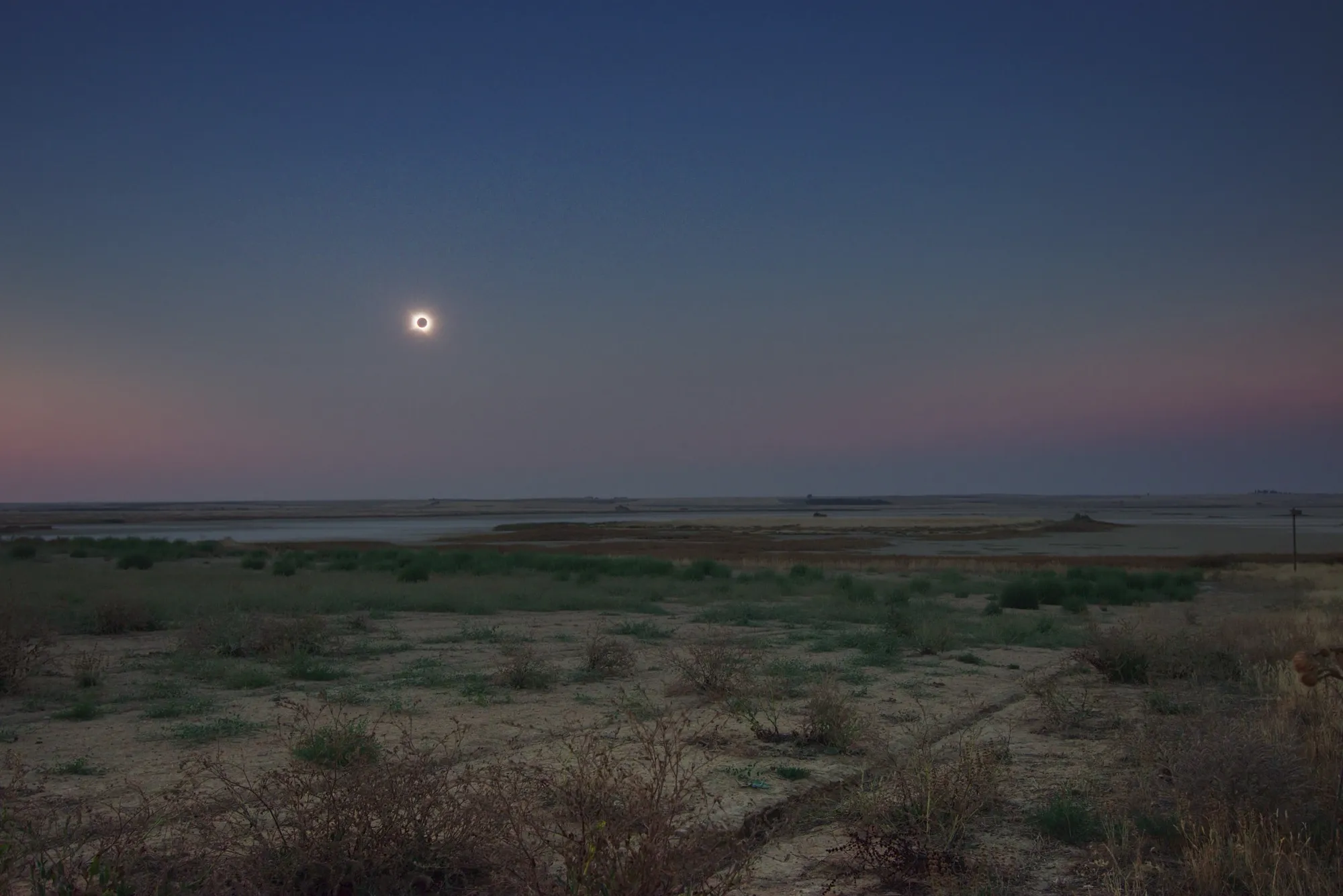 La corona solar sobre la laguna de Villafáfila durante la totalidad, con el horizonte encendido en tonos rosados en todas direcciones