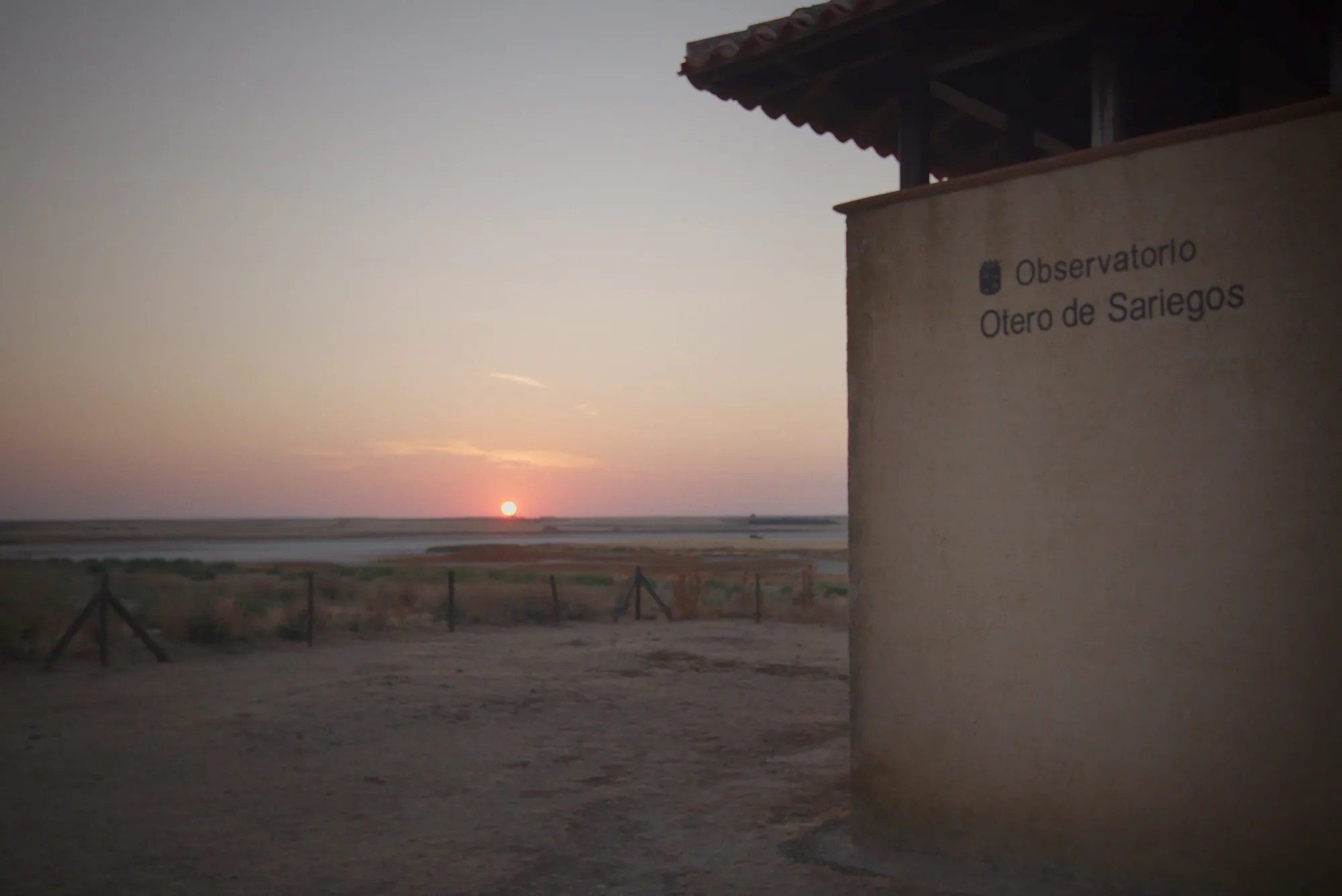 La puesta de sol sobre la laguna desde el observatorio de Otero de Sariegos, con el rótulo del edificio en primer plano